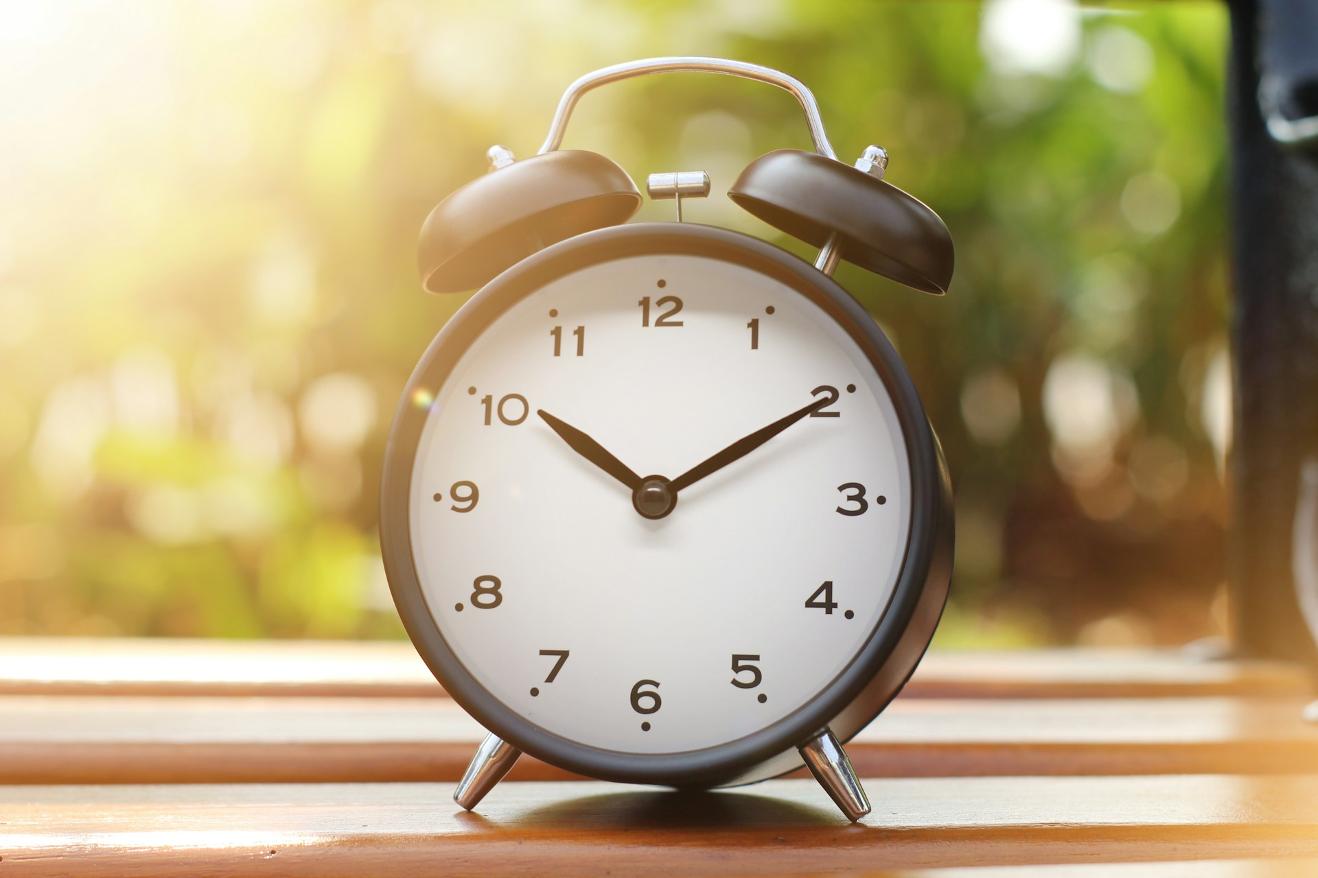 A black and white alarm clock on a wooden table in warm morning sunlight.