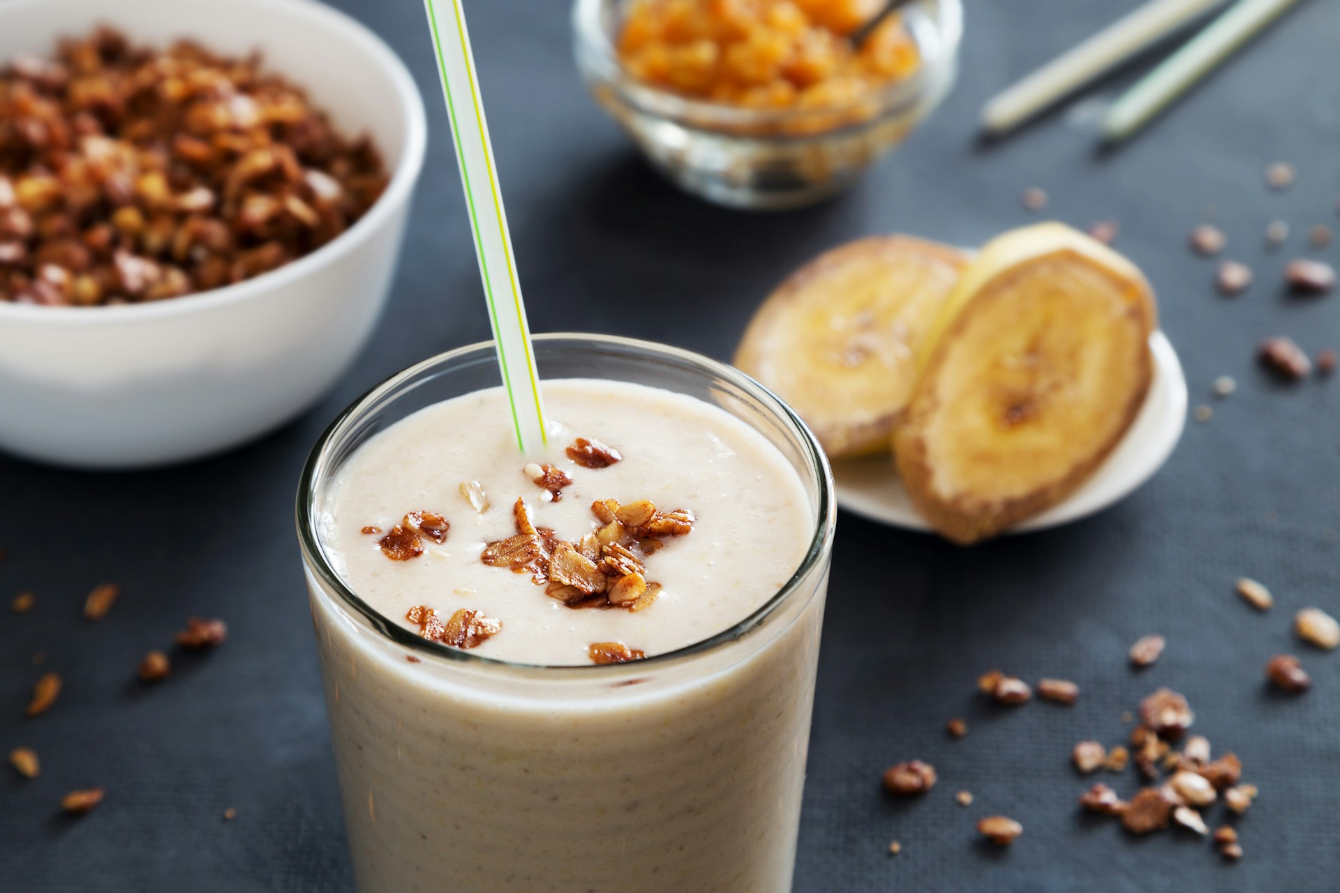 A banana smoothie in a glass next to a a bowl of nuts.