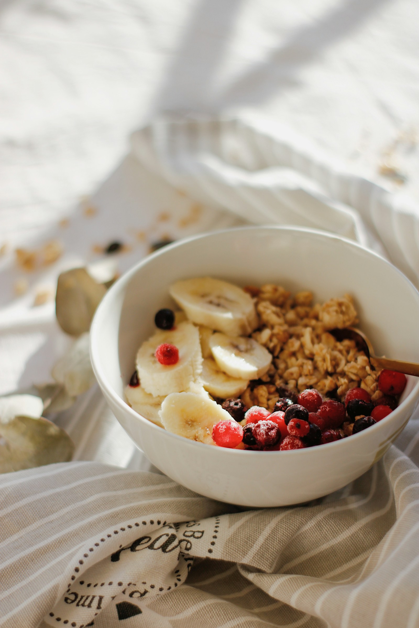 A breakfast bowl with granola, banana, and berries on a softly lit table.