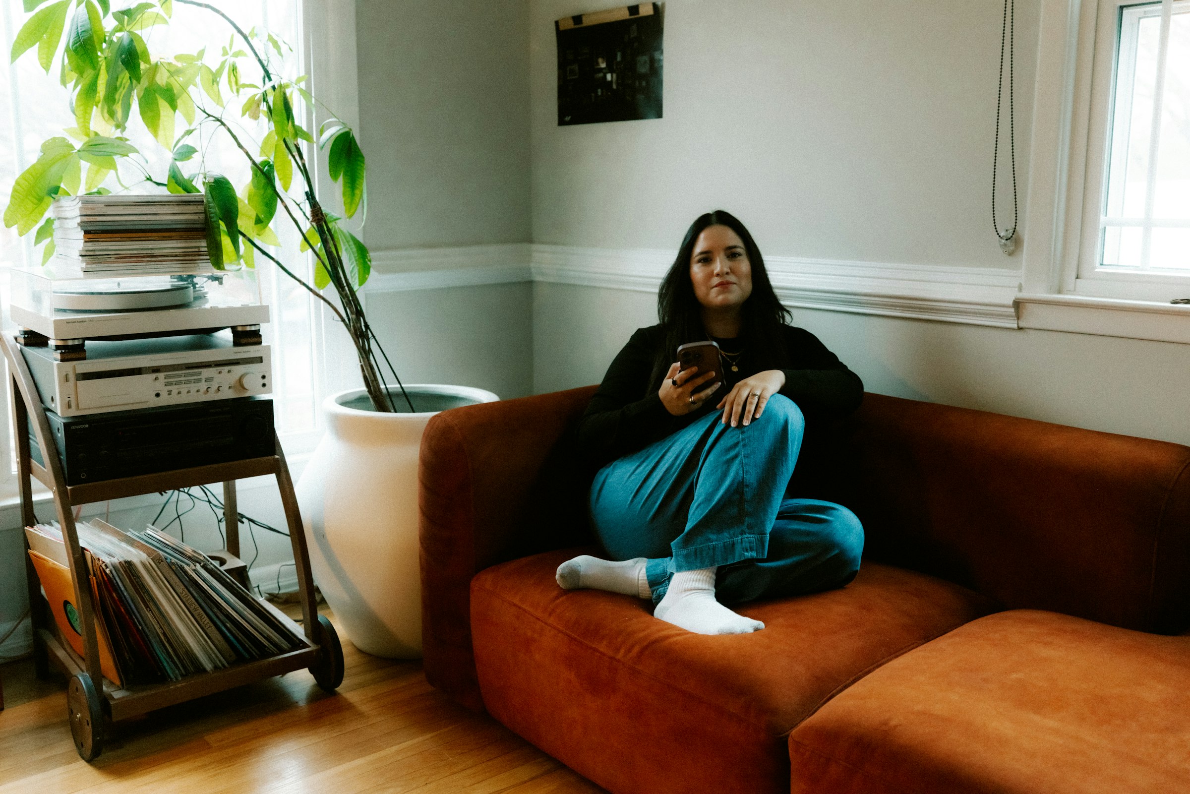 A woman sitting cross-legged on a couch at home, looking at her phone.