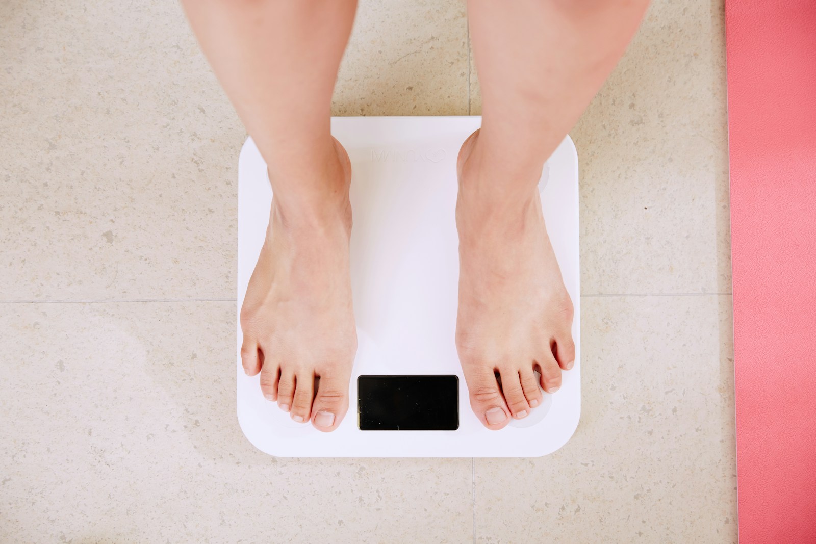 Bare feet standing on a white digital bathroom scale on a tiled floor.