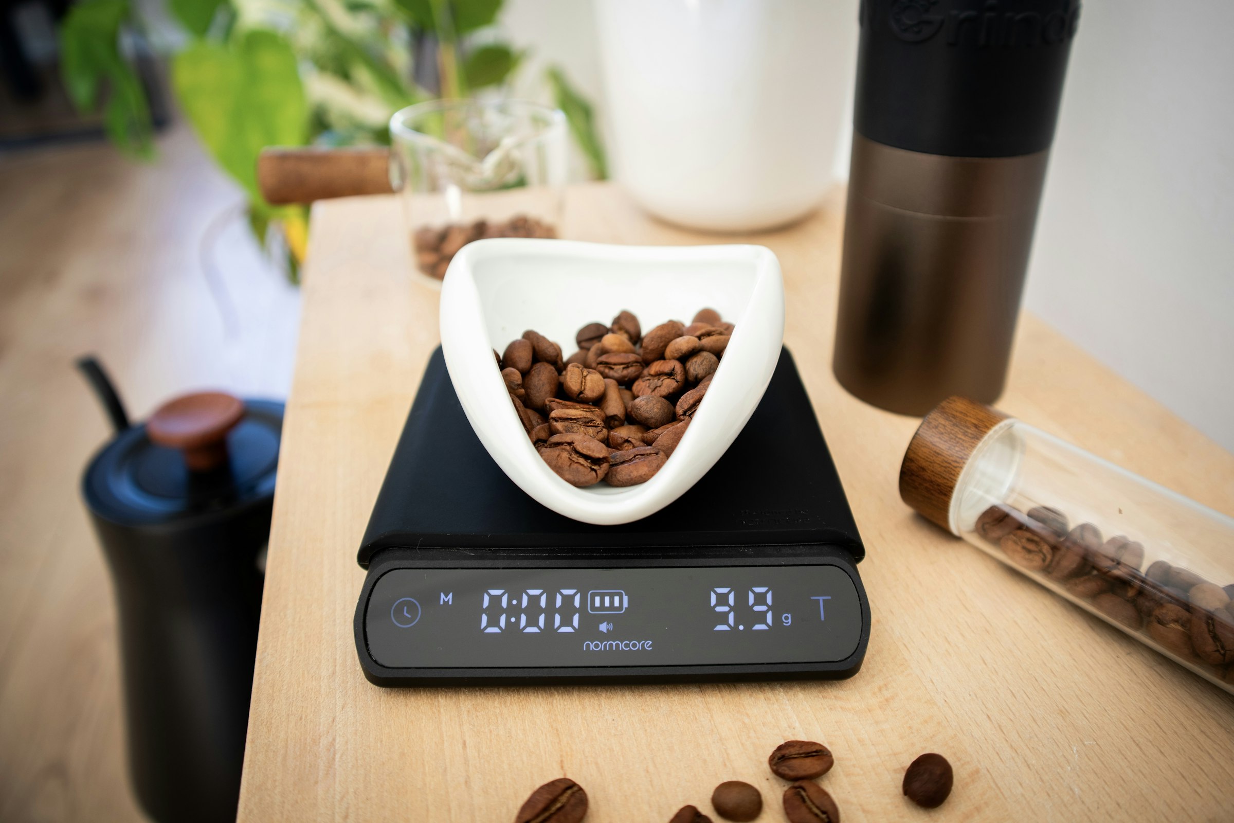 A white bowl of coffee beans resting on a black digital kitchen scale on a wooden worktop.