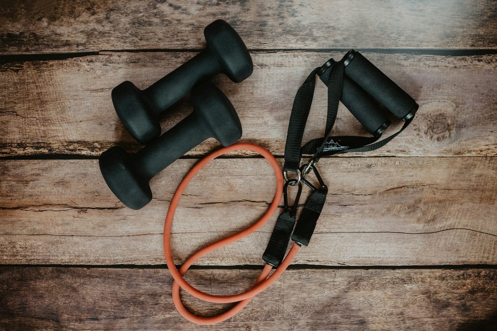 Two small dumbbells and a resistance band on a wooden floor, ready for a home workout.