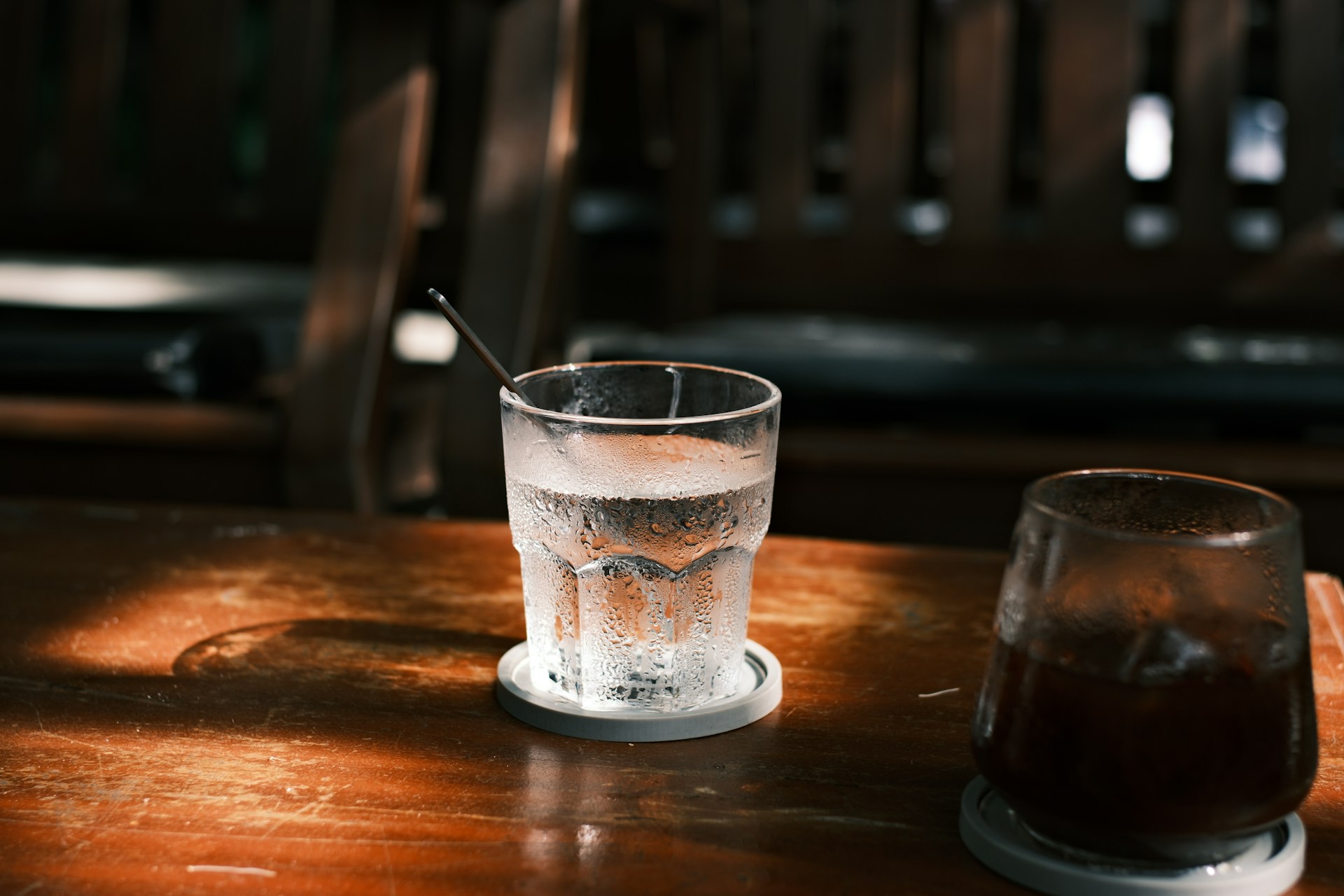 A glass of iced water next to a dark fizzy drink on a wooden table.