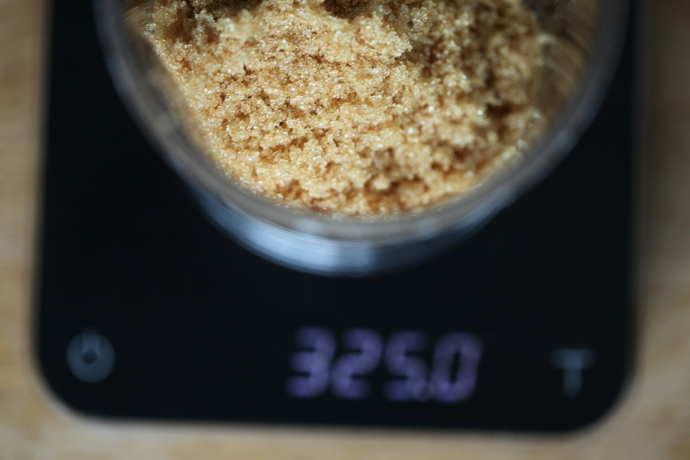 A measuring cup of brown sugar being weighed on a digital kitchen scale.