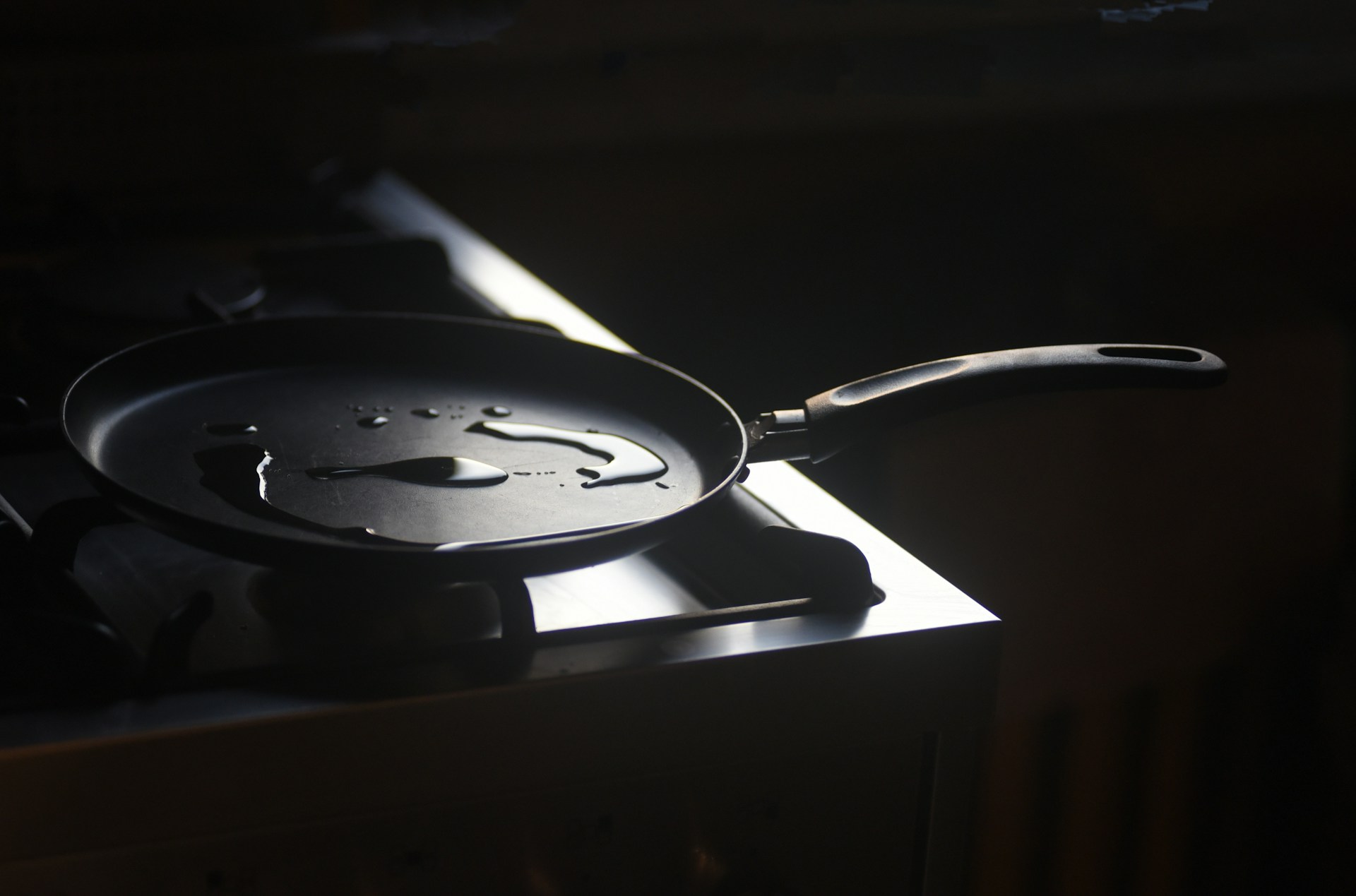 Light catching a little cooking oil in a dark frying pan on a stove.
