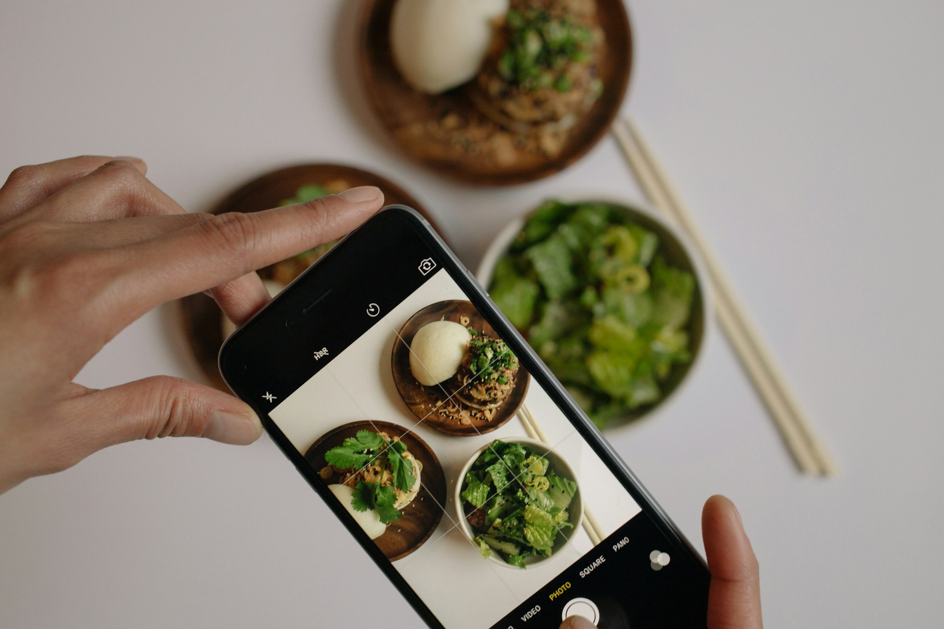 Hands holding a phone above the table to photograph three bowls of food.