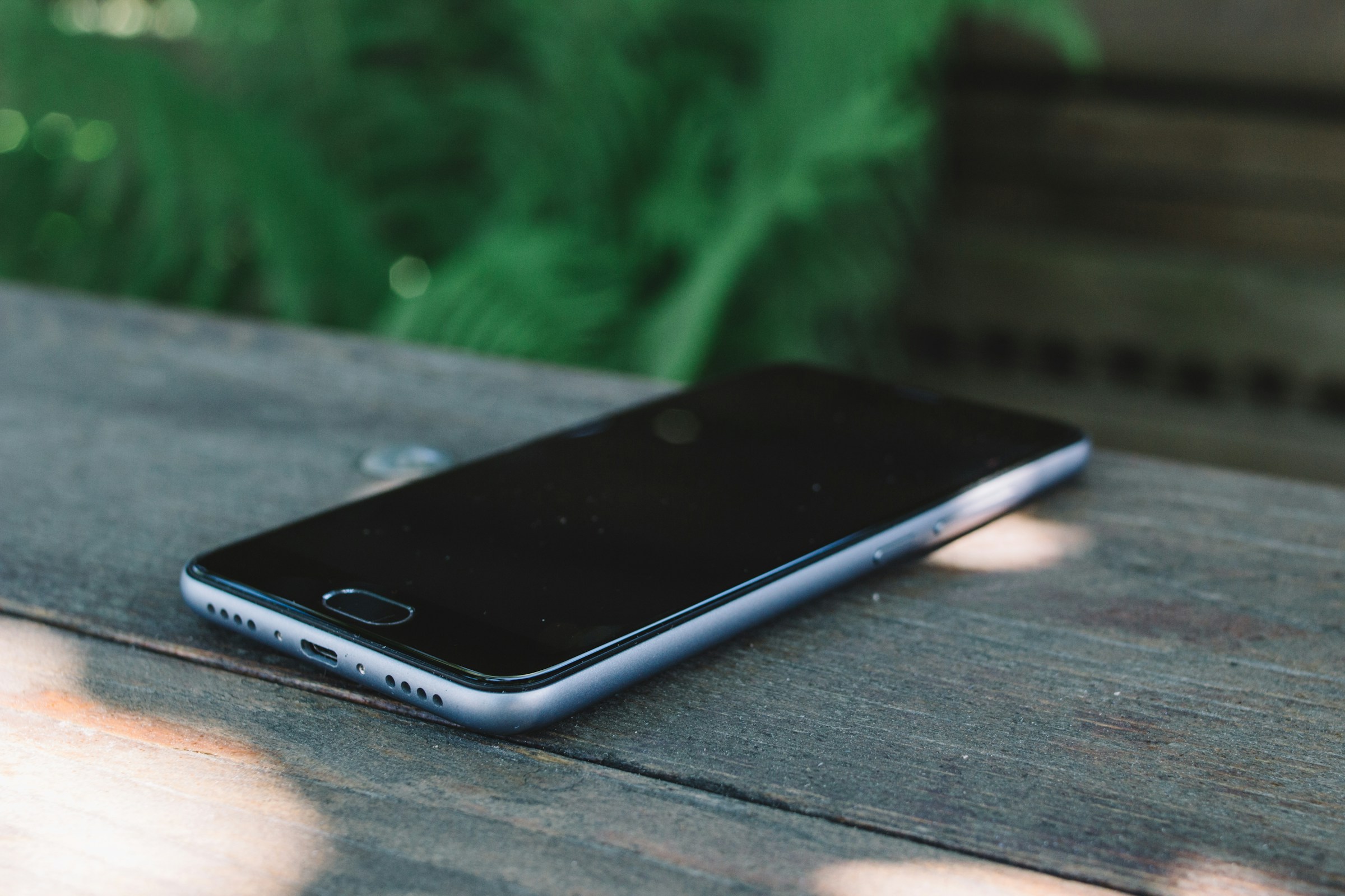 A smartphone with its screen off, resting on a wooden table outdoors.