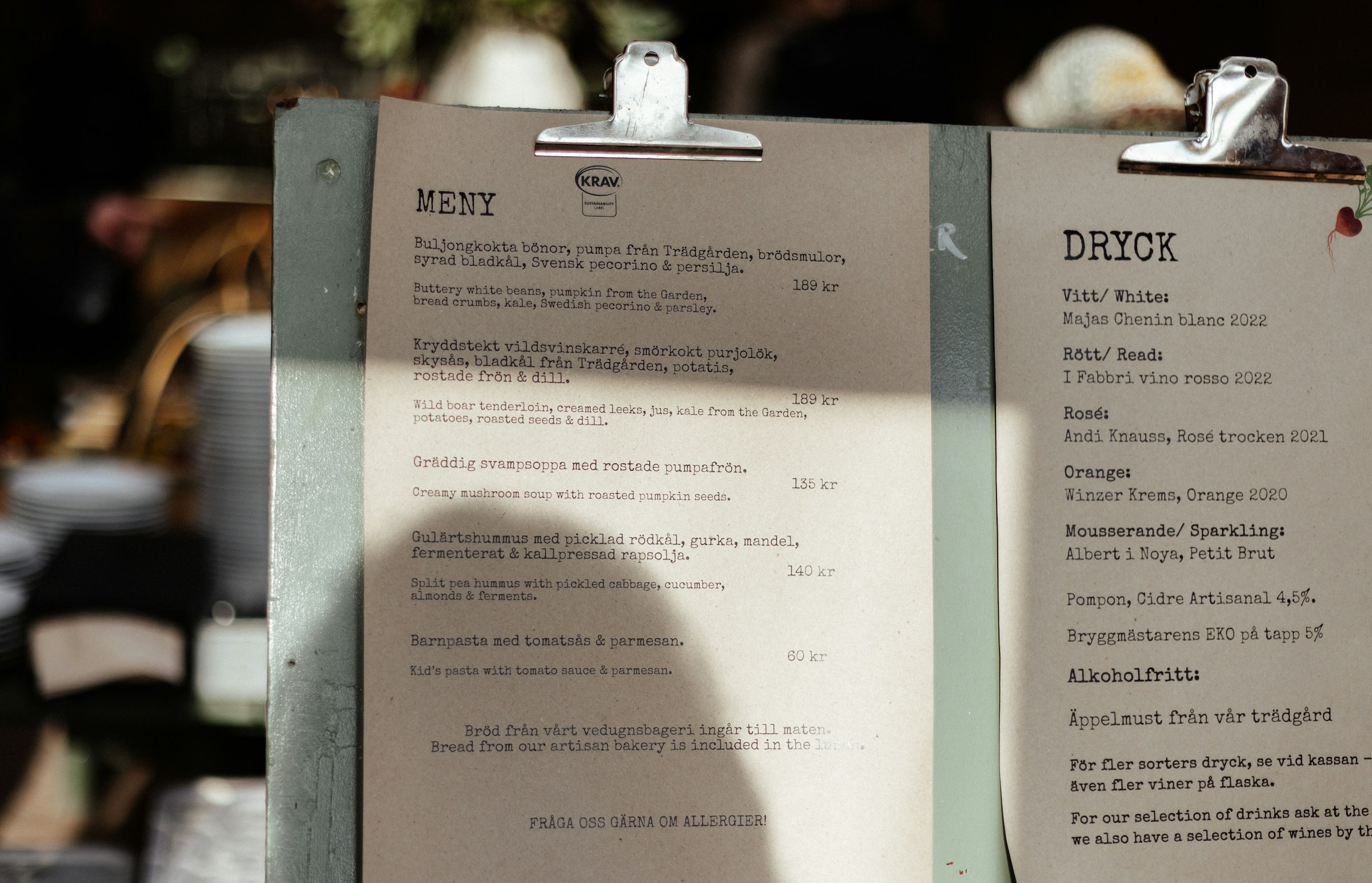 A printed café menu clipped to a board, showing food and drink items with their prices.