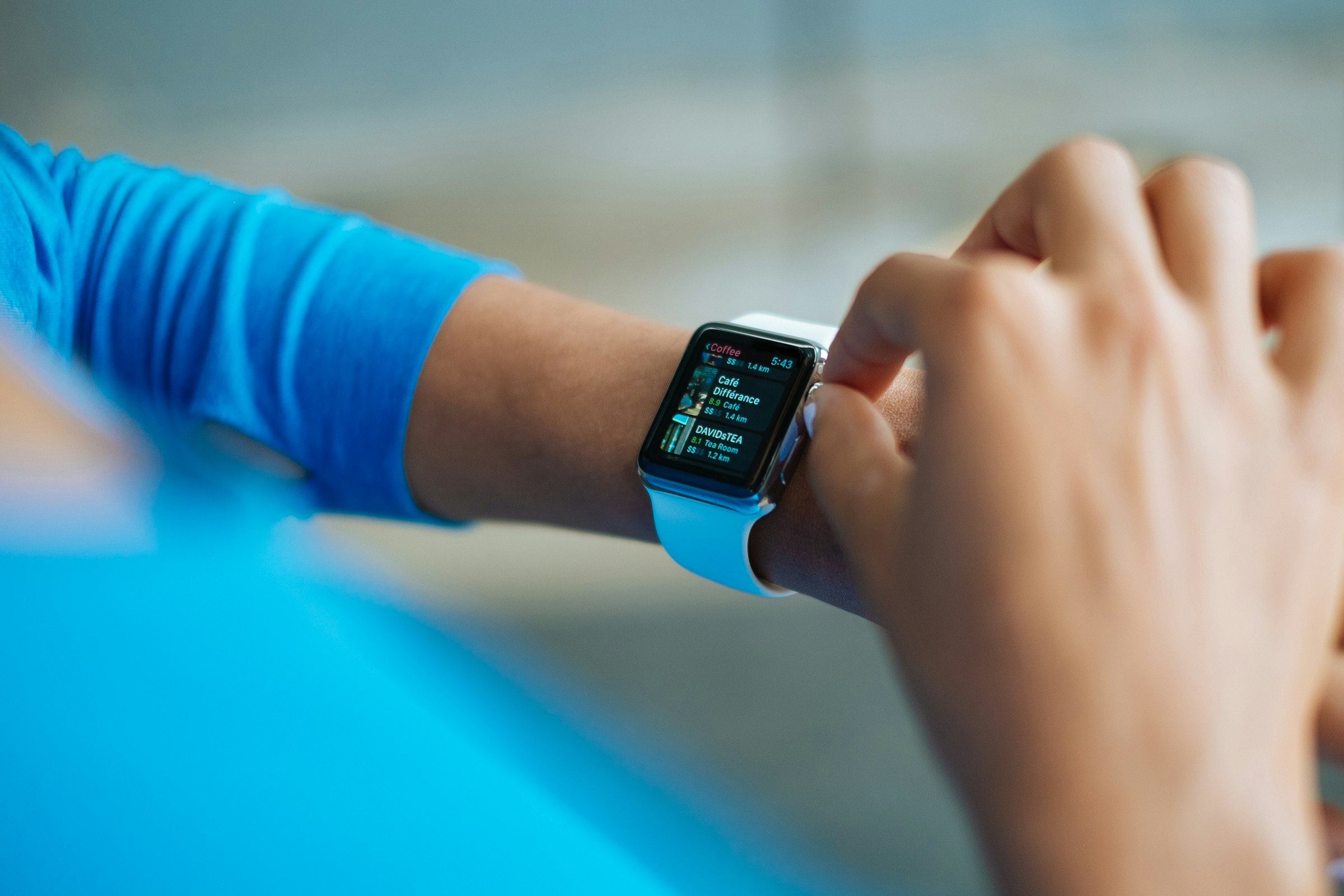 A person in a blue sports top tapping the screen of a smartwatch on their wrist.