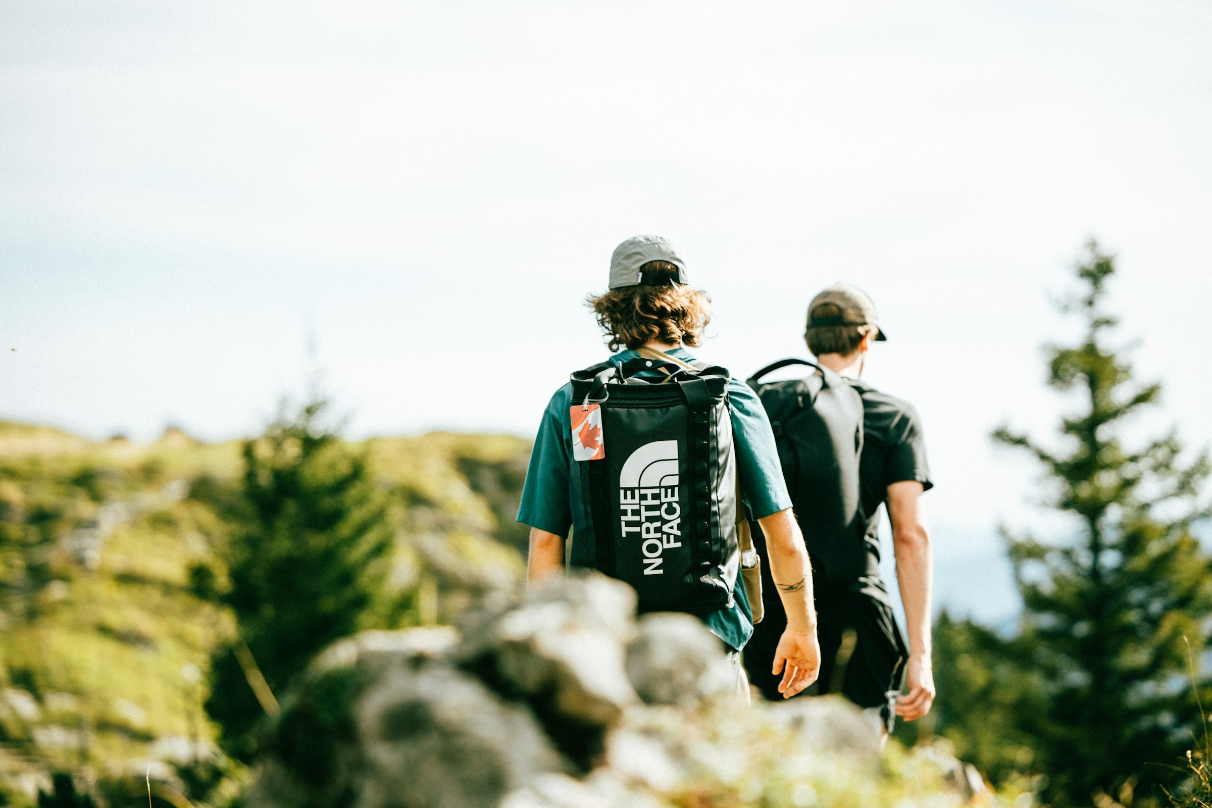 Two hikers walking a sunlit trail together, one slightly ahead of the other.