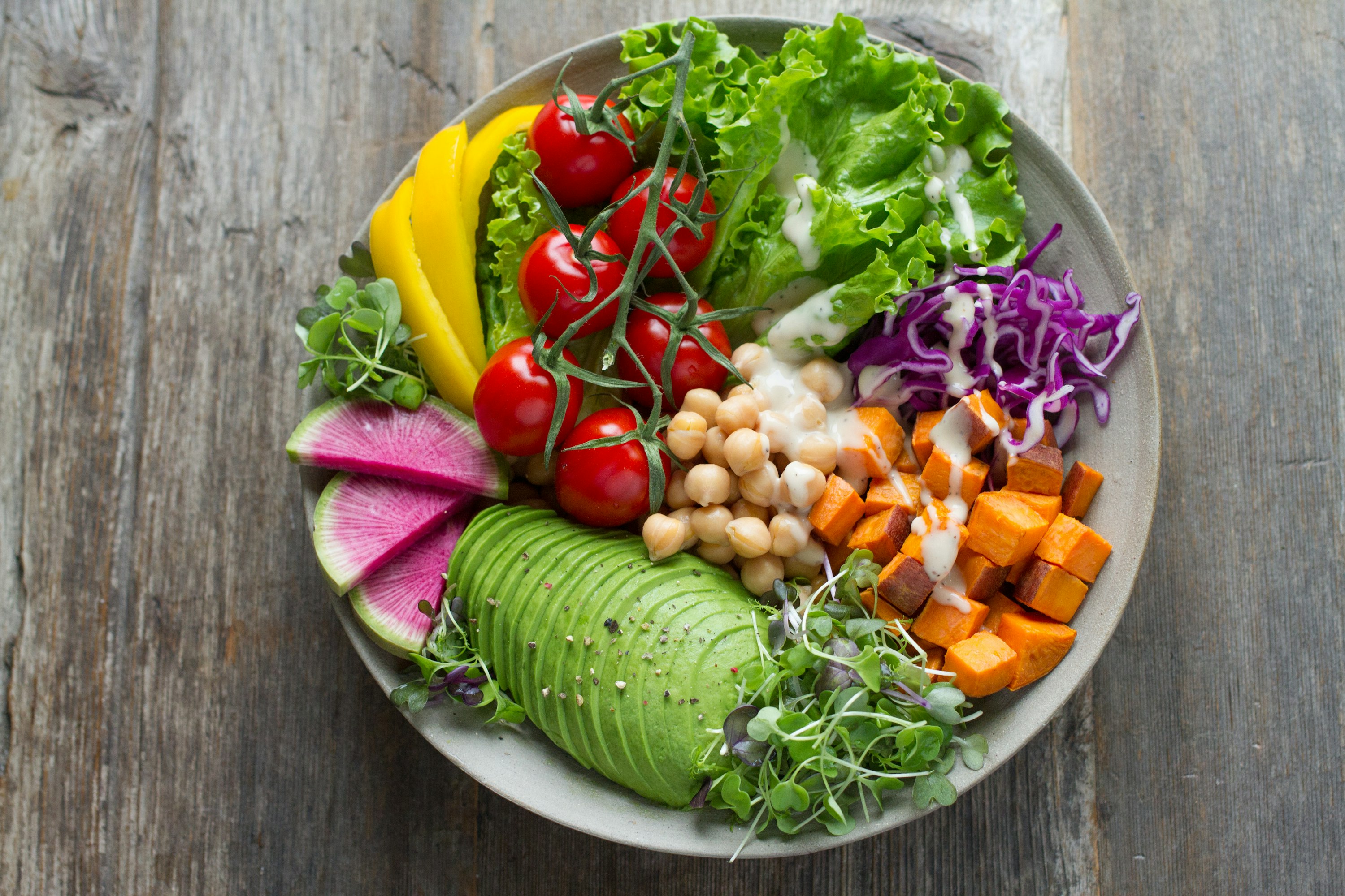 A colourful bowl with avocado, chickpeas, tomatoes, sweet potato, and leafy greens.