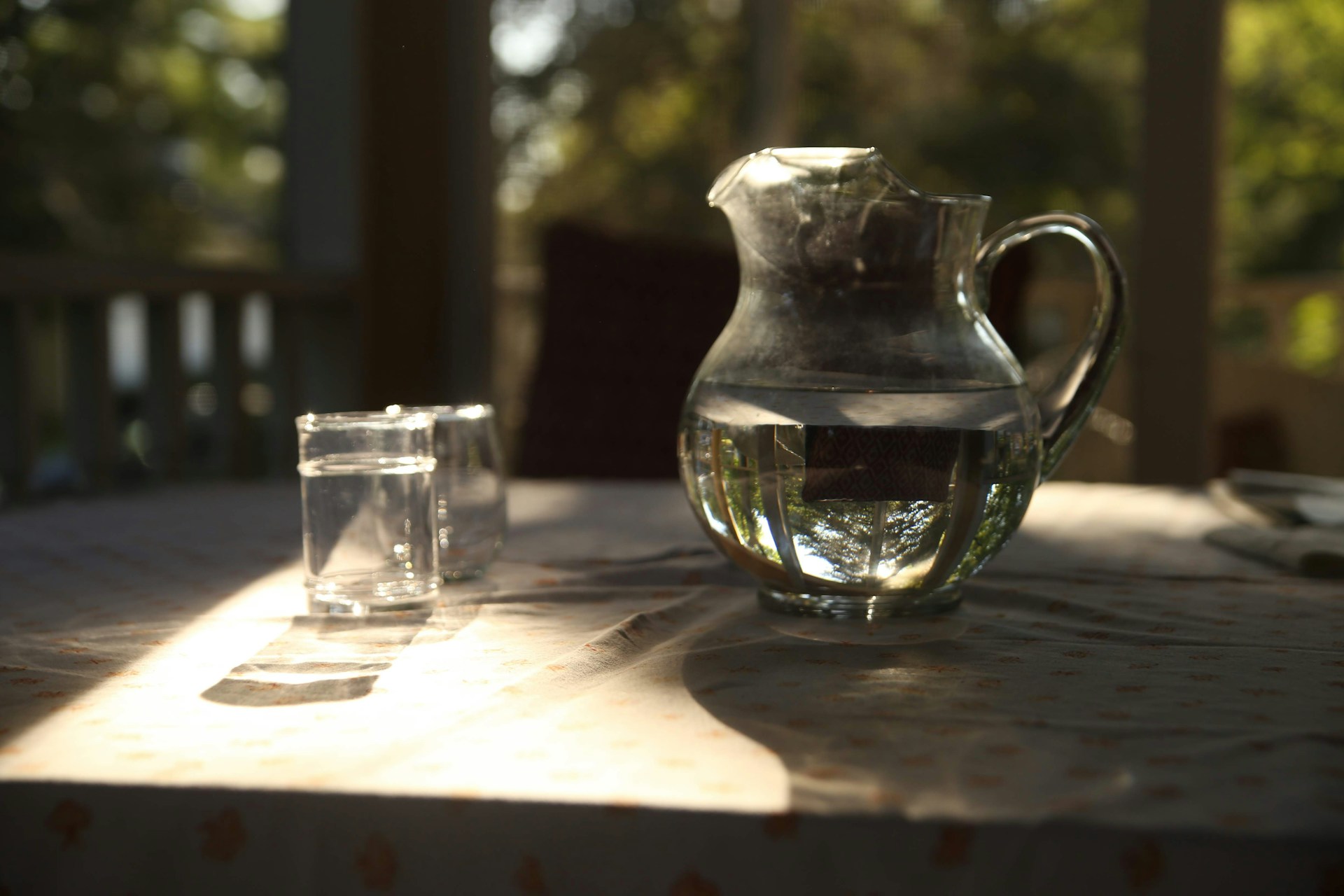 A glass jug of water next to a glass of water on a table.